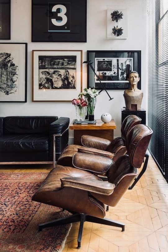 a chic mid-century modern living room with a black leather sofa, brown Eames loungers, a black and white gallery wall
