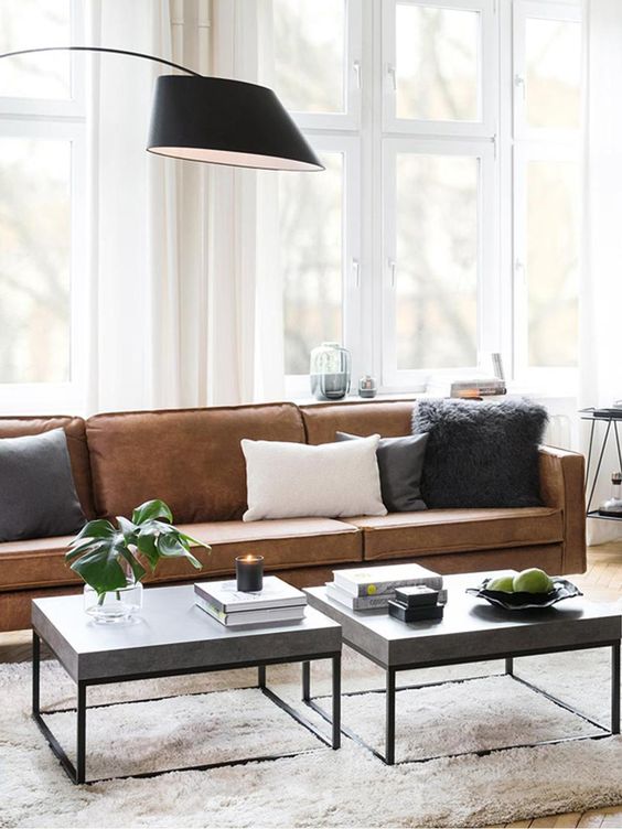 a chic modern living room with a brown leather sofa, grey coffee tables, monochromatic pillows and a black floor lamp