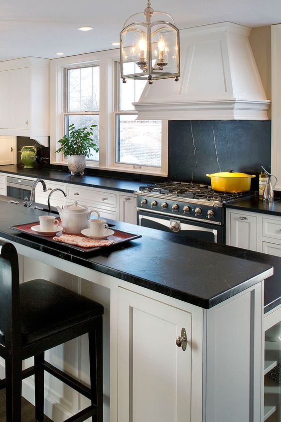 a chic neutral vintage kitchen with shaker cabinets, a large kitchen island, a black soapstone backsplash and countertops and hanging lamps