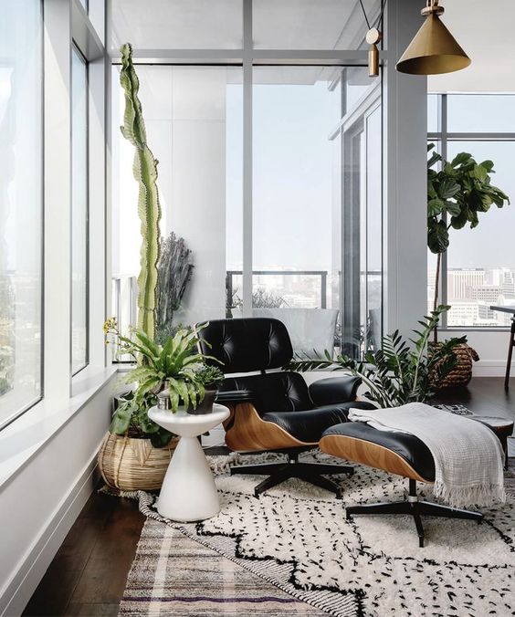 a chic nook with a black lounger and ottoman, a printed rug, potted greenery around is a very cozy space to read here