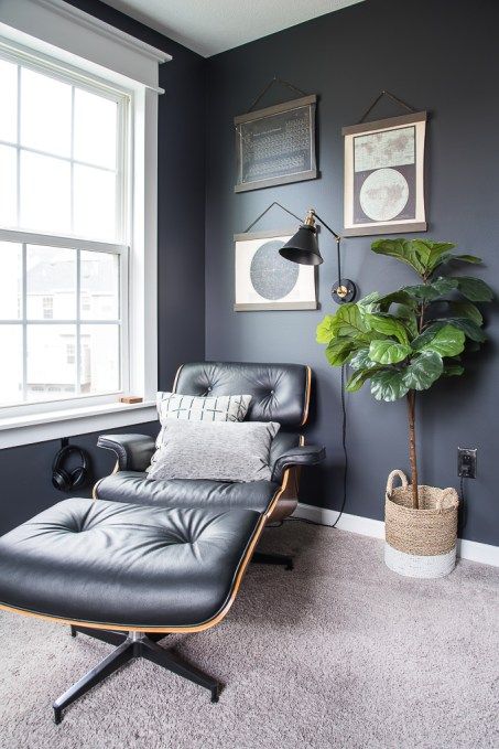 a chic nook with graphite grey walls, a black Eames lounger, a gallery wall, a potted plant and a black sconce