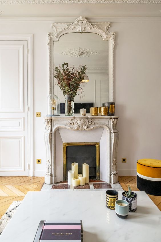a chic oranted mantel French fireplace with a matching mirror over the mantel, with candles and greenery plus a marble coffee table