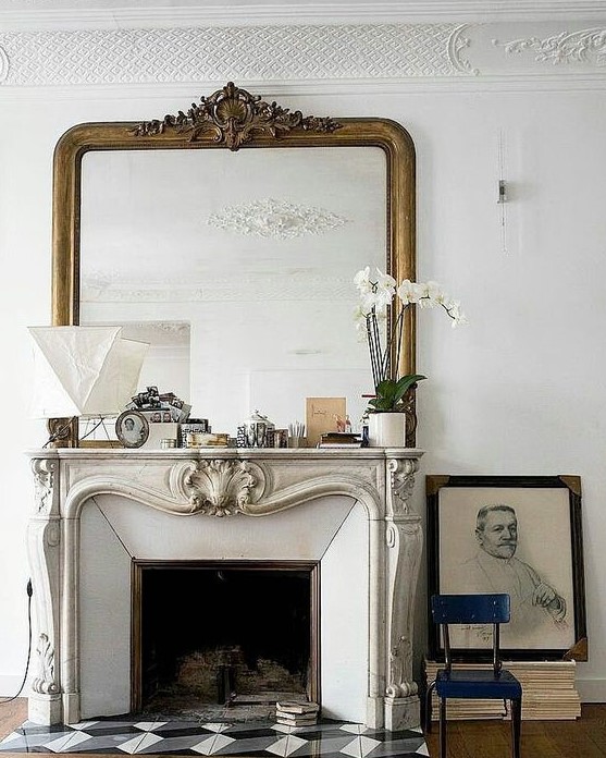 a chic vintage French fireplace with an ornated mantel, some pretty mantel decor, an oversized mirror and some books