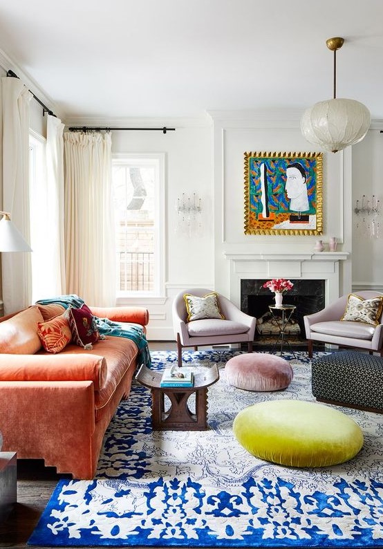 a colorful eclectic living room with a fireplace, lilac chairs, an orange velvet sofa, Moroccan furniture, a rug and poufs is bold