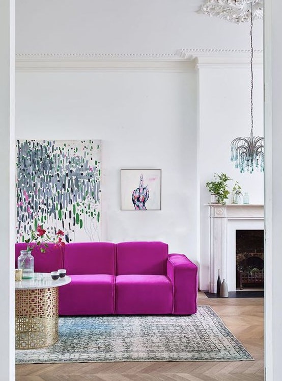 a contemporary living room with a fireplace, a hot pink sofa, cool artworks, a quirky chandelier, a printed rug and a chic table