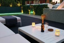 a contemporary outdoor space with smoked and charred oak decking, white upholstered furniture and a white low table, some built-in lights
