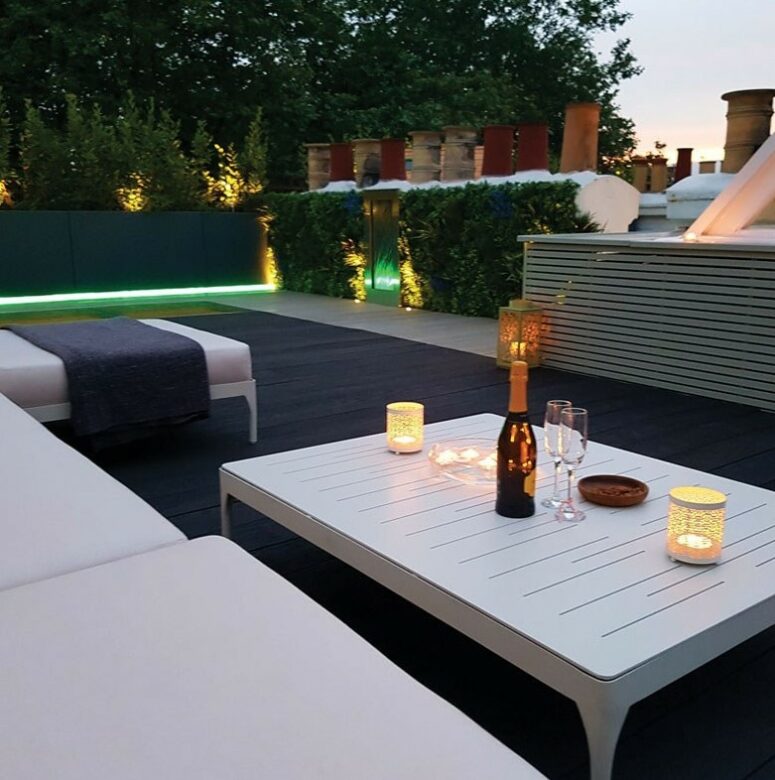 a contemporary outdoor space with smoked and charred oak decking, white upholstered furniture and a white low table, some built-in lights