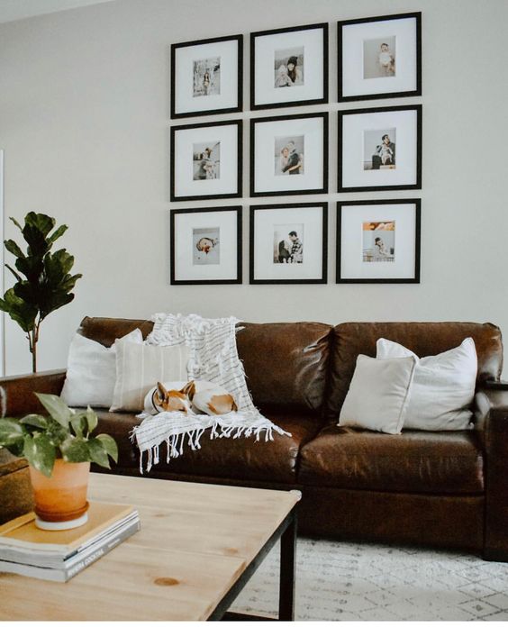 a cool boho living room with a brown leather sofa, a wooden coffee table, a grid gallery wall and potted greenery