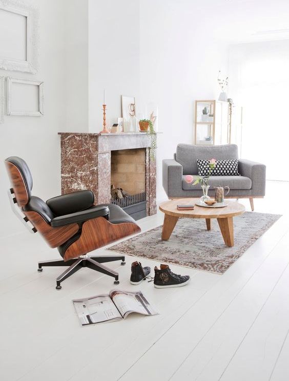 a cool fireplace nook with a marble clad fireplace, a grey chair and a black Eames lounger, a round coffee table and a rug