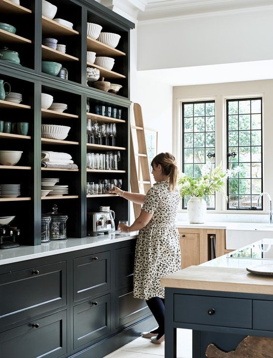 a cool large kitchen in navy, with open cabinetry and a large kitchen island, a stained cabinet and lots of natural light