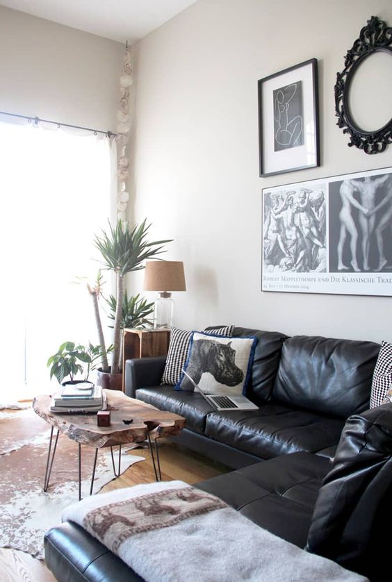 a cool living room with a black leather sectional, a living edge coffee table, a gallery wall and a cowhide rug