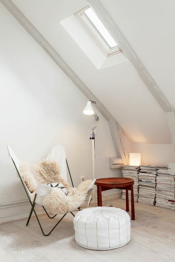 a cool reading attic nook with stacks of books and magazines, a white leather butterfly chair, a white Moroccan pouf and a floor lamp