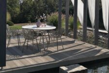 a cool terrace with a round table and woven chairs, with curtains, limed oak decking and rock steps placed right on the water