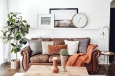 a cozy boho living room with a brown leather sofa and lots of pillows, a hairpin leg coffee table and baskets, a potted tree