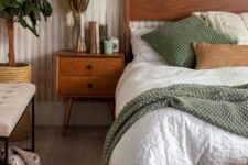 a cozy earthy bedroom with a stained bed and neutral bedding, a stained nightstand, an upholstered bench, a potted plant