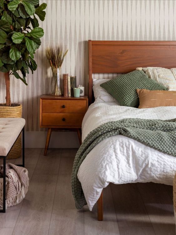 a cozy earthy bedroom with a stained bed and neutral bedding, a stained nightstand, an upholstered bench, a potted plant