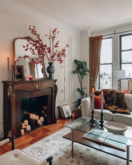 a cozy earthy-colored living room with a French fireplace with a stained mantel, a tiered coffee table, a white sofa and a neutral rug plus candles