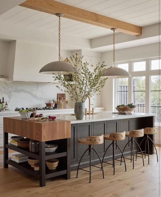 a cozy earthy kitchen with white cabinets and a black kitchen island, a small console table, tall stools and pendant lamps