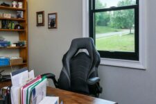a cozy farmhouse home office with a black frame double-hung window, a stained desk and a bookshelf, some books and decor
