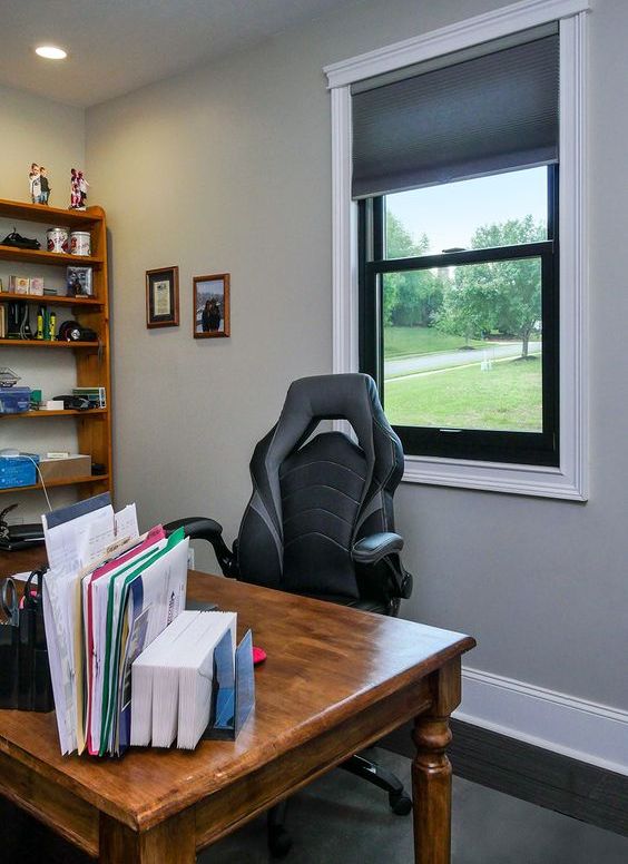 a cozy farmhouse home office with a black frame double hung window, a stained desk and a bookshelf, some books and decor
