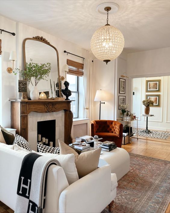 a cozy living room with a French fireplace with a refined stained mantel, neutral seating furniture and a rust chair, an oversized mirror