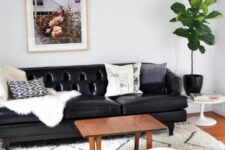 a cozy living room with a black leather sofa, a stained coffee table, a large rug and a white pouf, a potted statement plant