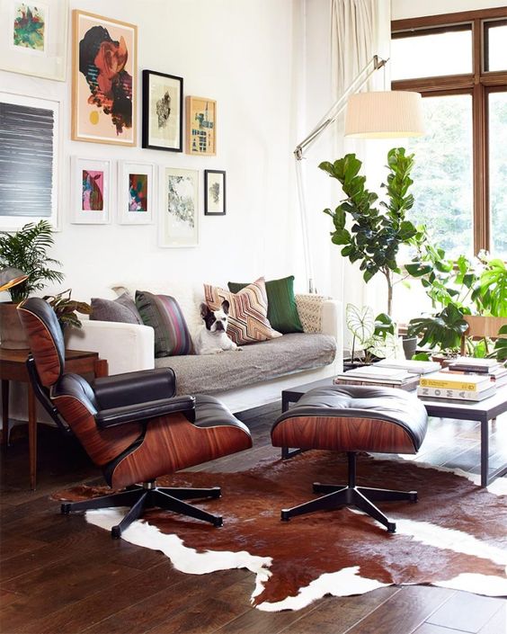 a cozy mid-century modern living room with a neutral sofa with printed pillows, a large gallery wall, a black Eames lounger and ottoman and a coffee table