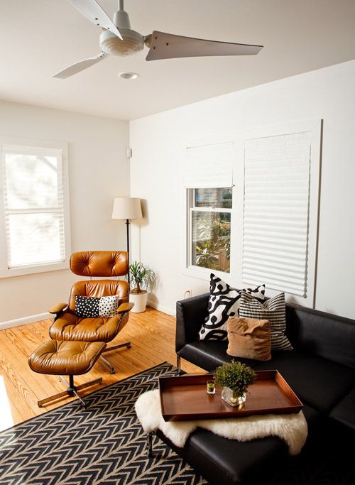a cozy modern boho living room with a black leather sofa and ottoman, a tan Eames lounger and an ottoman, a printed rug and pillows