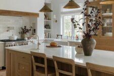 a cozy modern earthy kitchen with neutral lower cabinets, a large stained kitchen island, a large cupboard, a built-in hood and pendant lamps