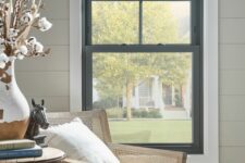 a cozy reading nook with a black frame double-hung window, a rattan chair, a side table and some books and decor