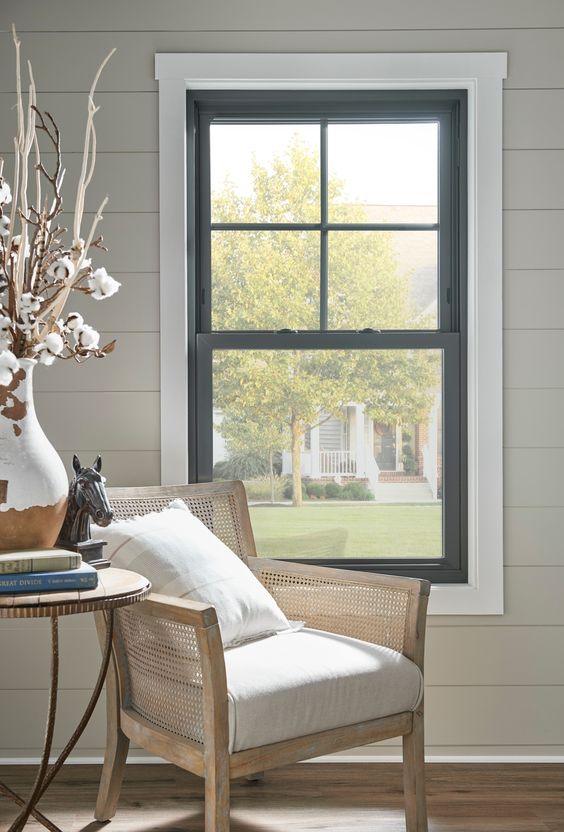 a cozy reading nook with a black frame double hung window, a rattan chair, a side table and some books and decor