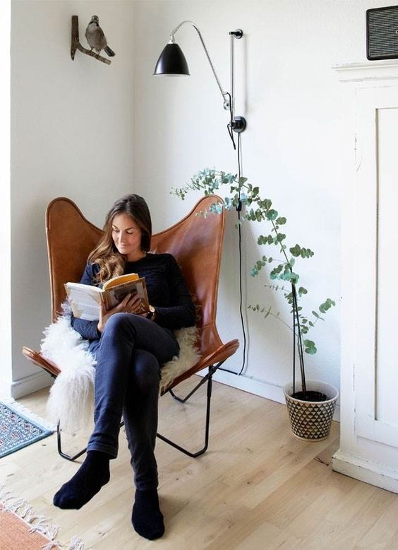 a cozy reading nook with a brown butterfly chair, faux fur, a potted plant, a black wall sconce is amazing