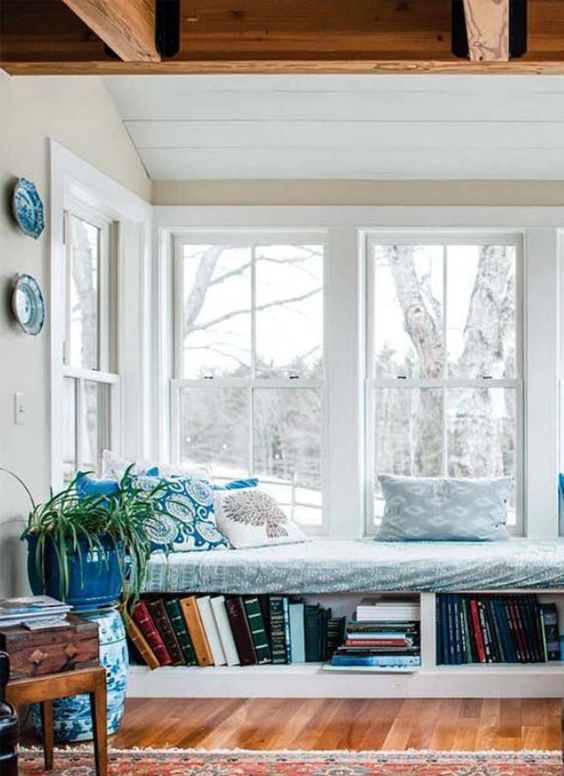a cozy reading nook with a series of double hung windows, a windowsill daybed with book storage and some printed decor