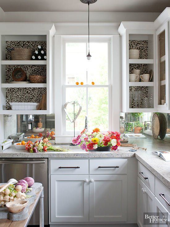 a cozy white kitchen with shaker and open cabinets with wallpaper backing, white terrazzo countertops and black handles