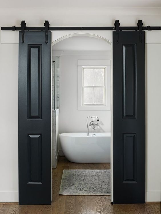 a farmhouse bathroom with black sliding barn doors, an oval tub, a double hung window and a shower space