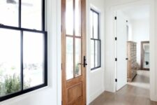 a farmhouse entryway with black double-hung black frame windows, a stained door and white walls with trim