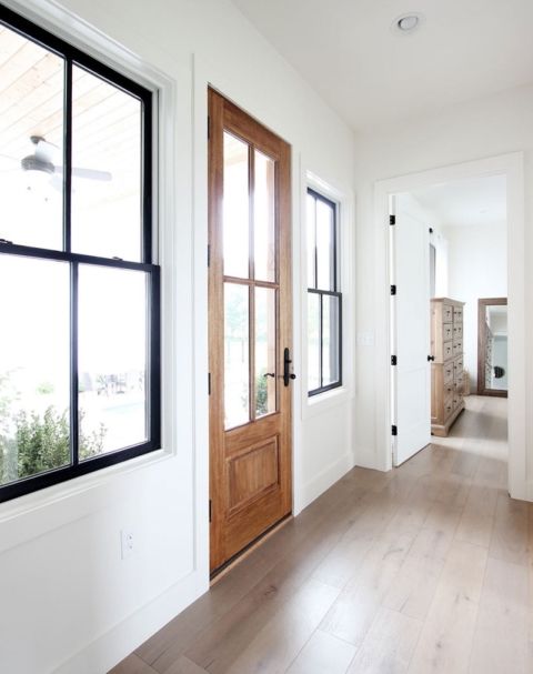 a farmhouse entryway with black double hung black frame windows, a stained door and white walls with trim