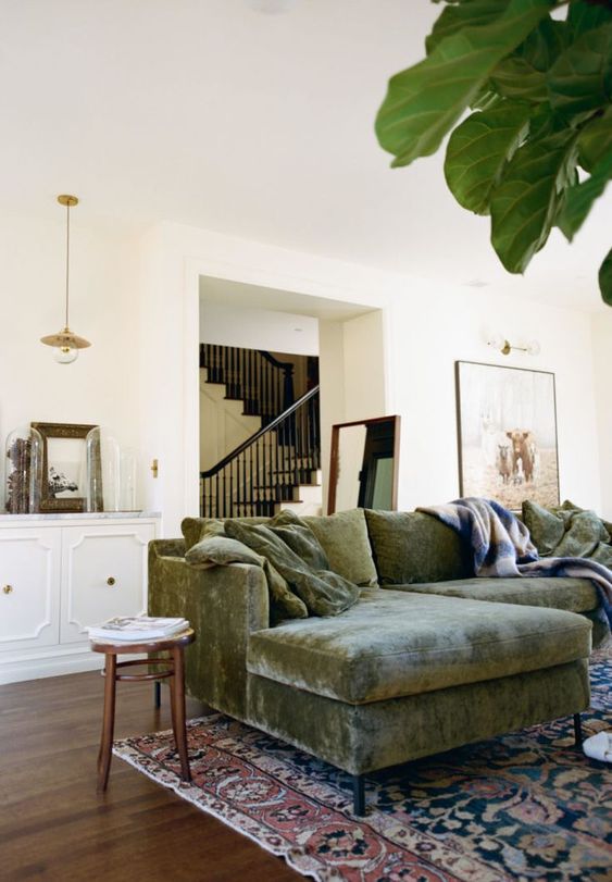 a farmhouse living room with a green velvet sectional, a boho printed rug, a white credenza with some decor and stained stools