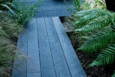 a garden with brushed basalt millboard decking, greenery and grass around and a bowl with water and a wooden lid