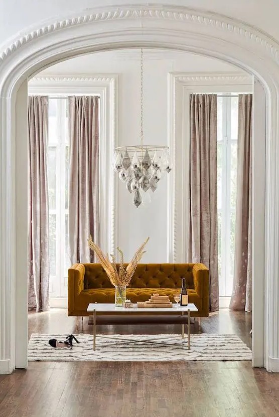 a glam living room with a chandelier, a mustard velvet sofa and blush velvet curtains create a gorgeous ambience