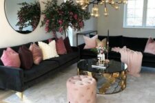 a glam living room with black sofas, pink and mauve pillows, a gold bulb chandelier, a black and gold coffee table and a pink pouf