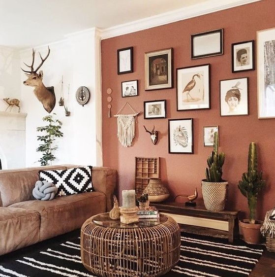 a gorgeous boho living room with a terracotta wall, a gallery wall, some cacti in pots, a leather sofa and a wooven table