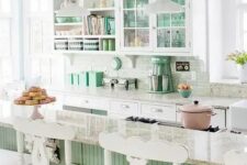 a gorgeous coastal kitchen done in white, light green and aqua, with glass and open cabinets, a green kitchen island and white stools