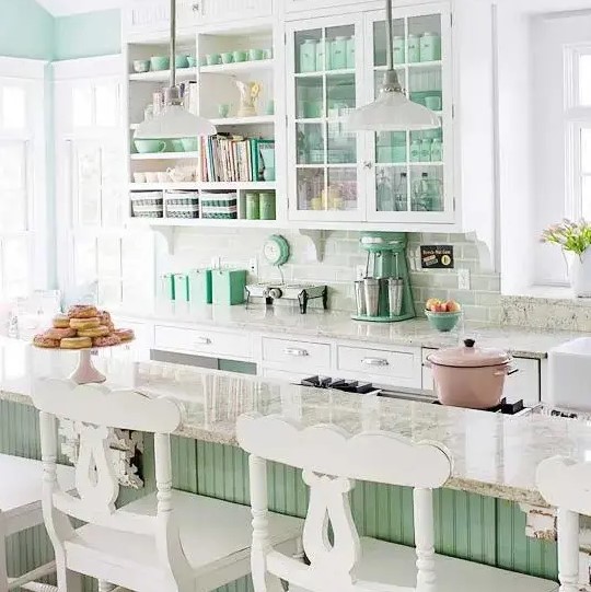 a gorgeous coastal kitchen done in white, light green and aqua, with glass and open cabinets, a green kitchen island and white stools