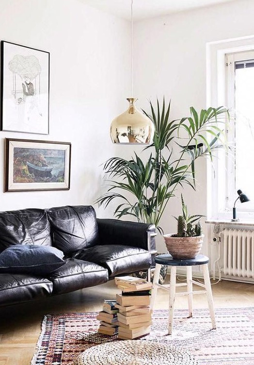 a gorgeous contemporary living room with a black leather sofa, stacks of books, potted plants and a chic gallery wall
