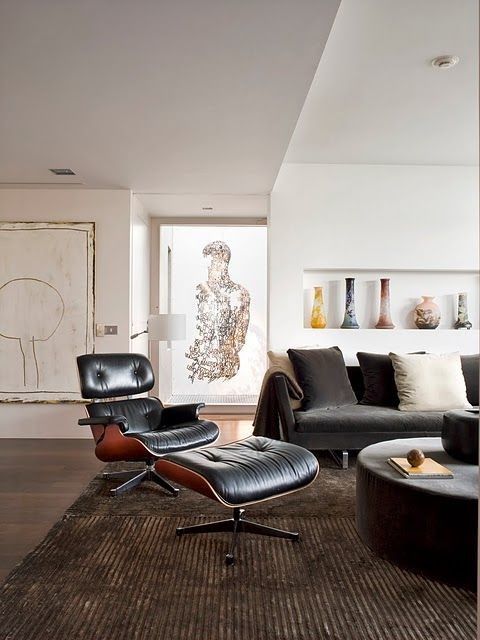 a gorgeous living room with a black sofa, a black Eames lounger, a round coffee table, a niche with vases and lots of art
