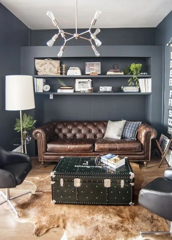 a grey living room with a brown leather Chesterfield, black chairs, a black chest as a coffee table and an animal skin rug