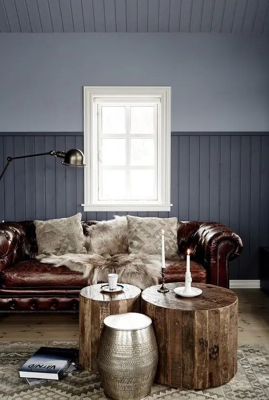 a grey living room with a brown leather Chesterfield sofa, wooden stools and a metal one, candles and a lamp