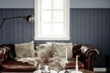 a grey living room with a brown leather Chesterfield sofa, wooden stools and a metal one, candles and a lamp