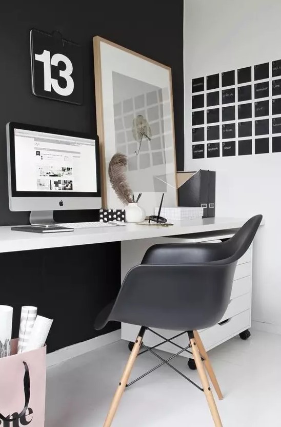 a laconic Nordic home office with a black statement wall and Eames chair, a black noteboard, a white desk and a relaxed artwork